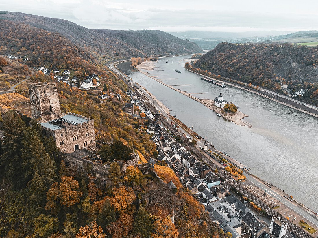 Aufnahme des Rheins in Vogelperspektive. Am Ufer ist eine Burg zu sehen, sowie eine kleine Stadt.