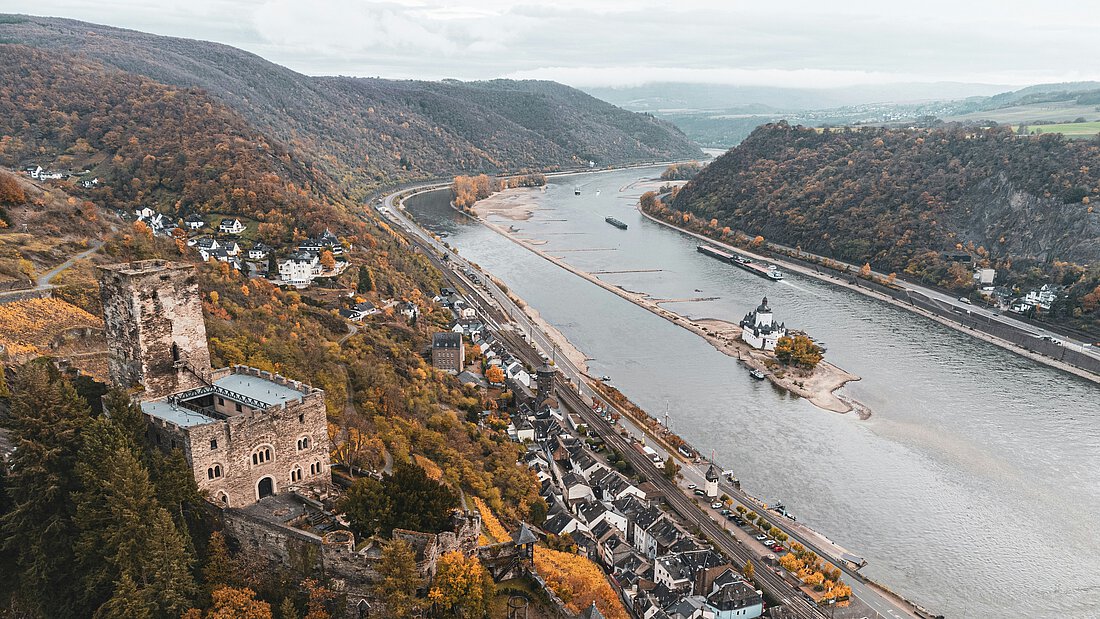 Aufnahme des Rheins in Vogelperspektive. Am Ufer ist eine Burg zu sehen, sowie eine kleine Stadt.