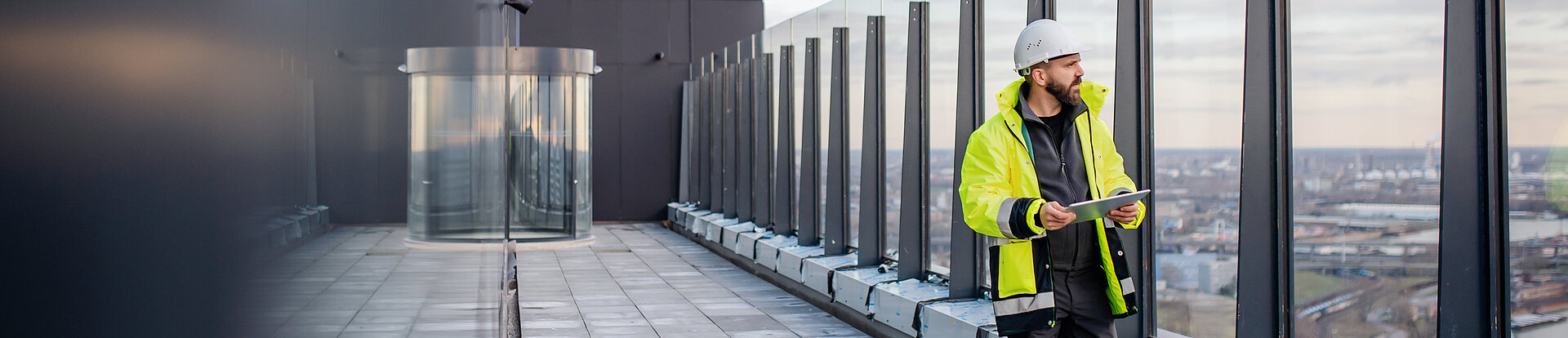 Ein Ingenieur schaut von dem Balkon eines modernen Gebäudes über eine Stadt.