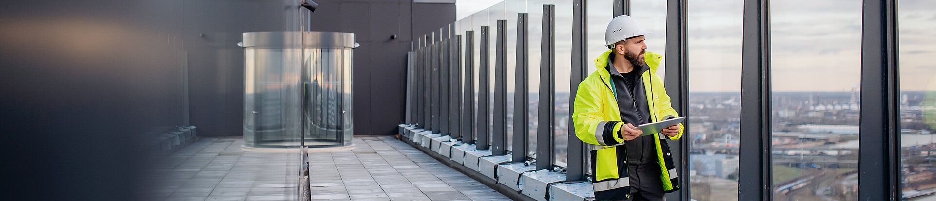 Ein Ingenieur schaut von dem Balkon eines modernen Gebäudes über eine Stadt.