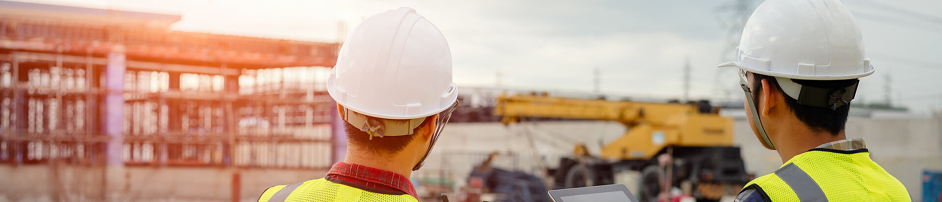 Zwei Ingenieure oder Bauarbeiter stehen vor einem Gebäude und fliegen eine Drohne darüber.