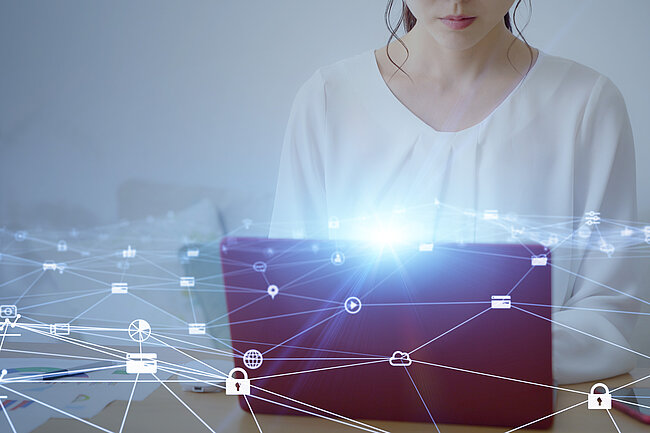  Eine Frau arbeitet an einem Laptop, wobei das Bild von digitalen Symbolen überlagert wird, die ein Netzwerk darstellen und auf das Konzept der Konnektivität im Geschäftsleben hinweisen.