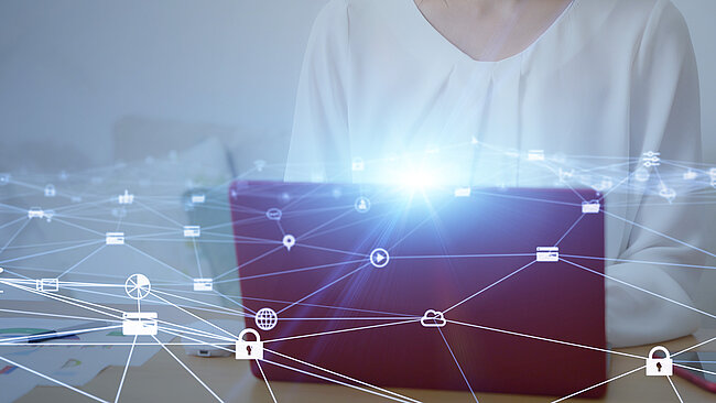  Eine Frau arbeitet an einem Laptop, wobei das Bild von digitalen Symbolen überlagert wird, die ein Netzwerk darstellen und auf das Konzept der Konnektivität im Geschäftsleben hinweisen.